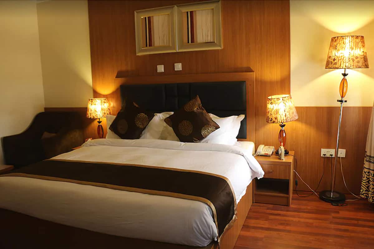Una habitación de hotel con una cama grande, dos lámparas de noche, una mesita de noche con teléfono y un cabecero de madera.