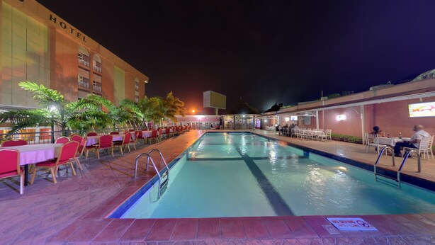 Zona de piscina de hotel con mesas y sillas, una piscina y un edificio con un cartel que dice "HOTEL".