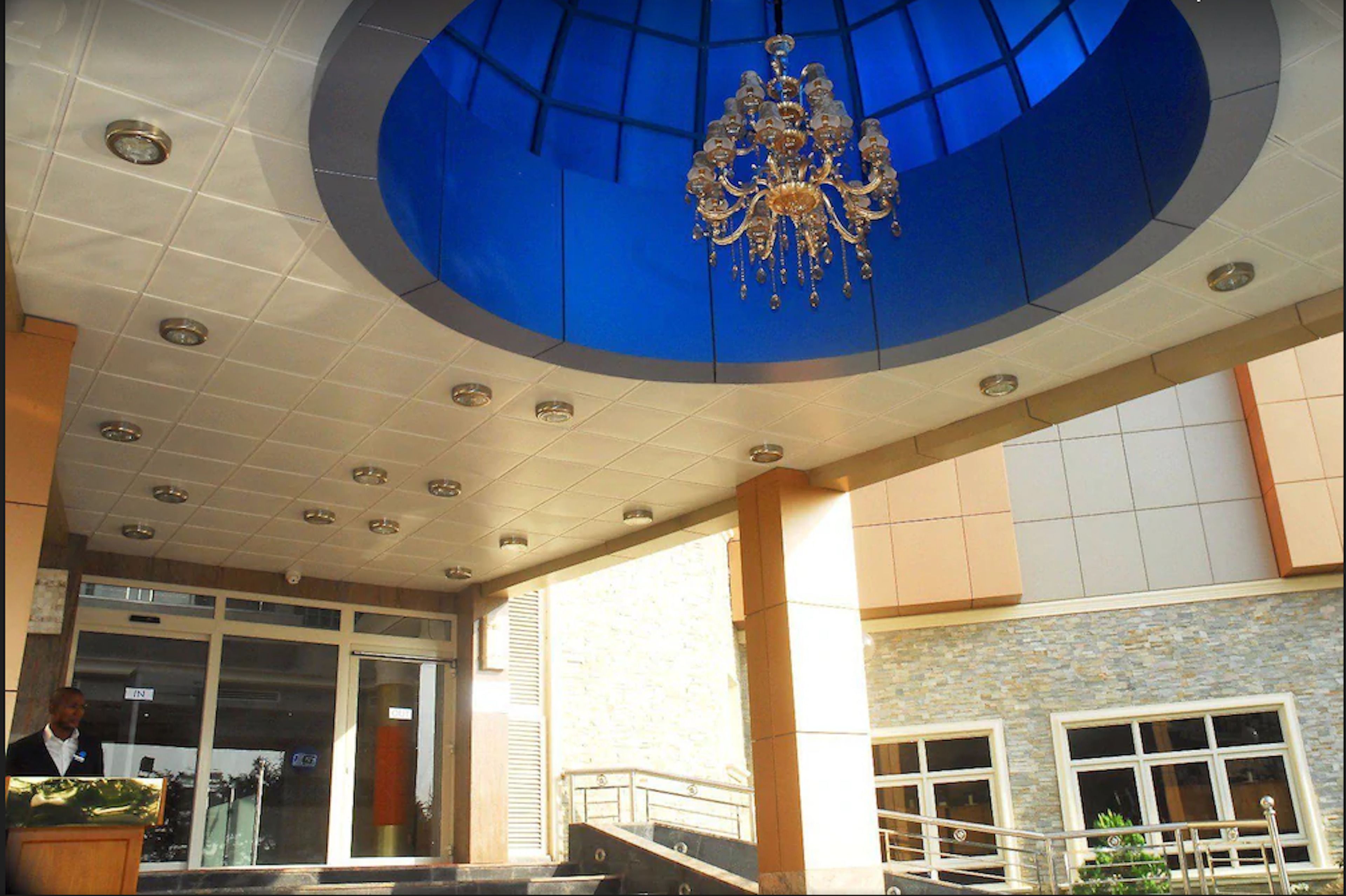 A hotel lobby with a blue-tiled ceiling, a chandelier, and a staircase leading to an upper floor.