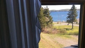 A window with a view of a grassy area, trees, and a body of water. - B&B Le Manoir du vieux Presbytère (Port-Daniel-Gascons)