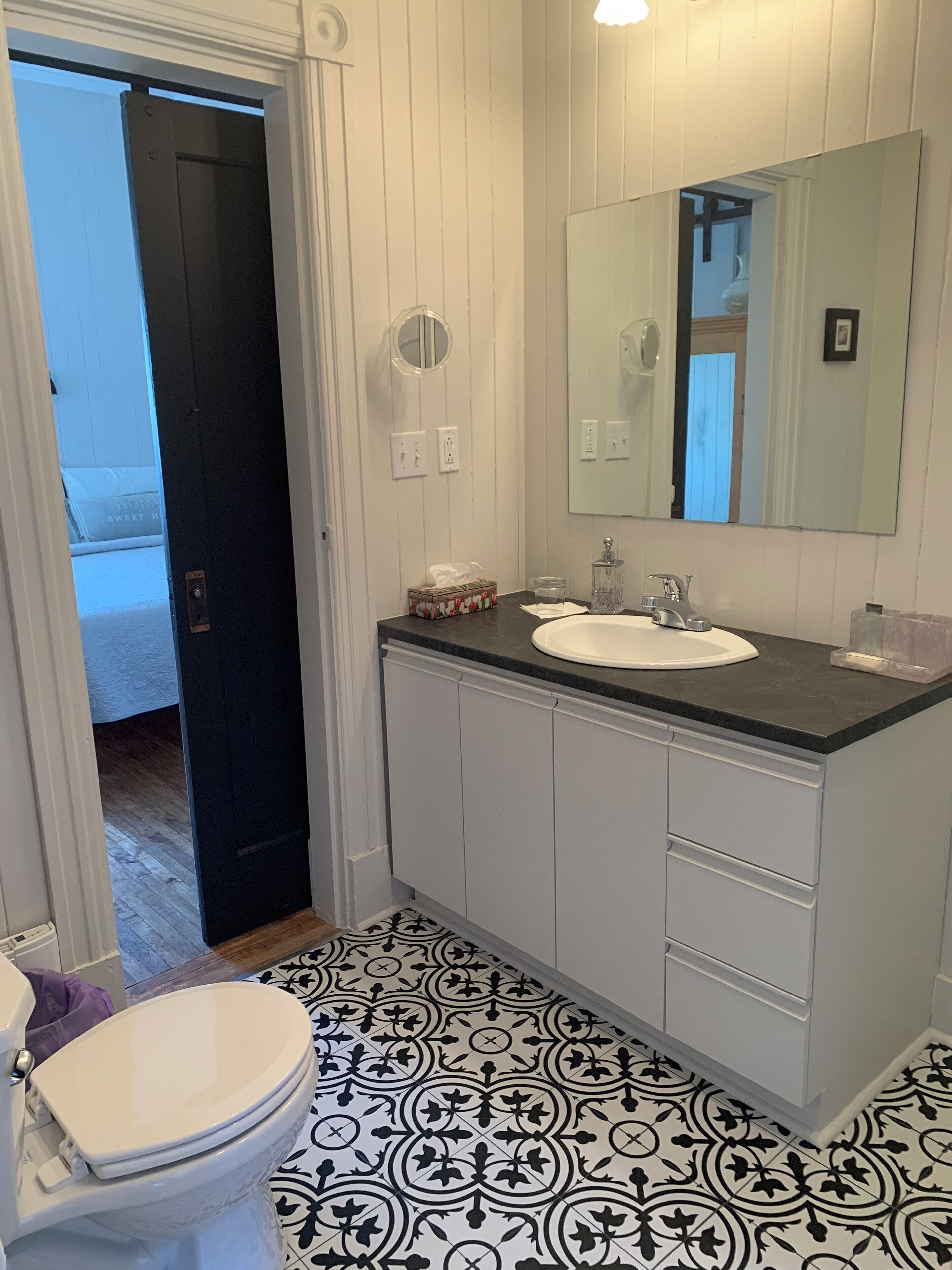 Ein Badezimmer mit Toilette, Waschbecken und einem Spiegel darüber, sowie Fliesenboden mit Muster.