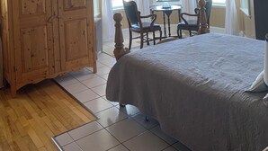 A bedroom with a large bed, wooden furniture, a ceiling fan, and a view of the outdoors through the windows. - B&B Le Manoir du vieux Presbytère (Port-Daniel-Gascons)