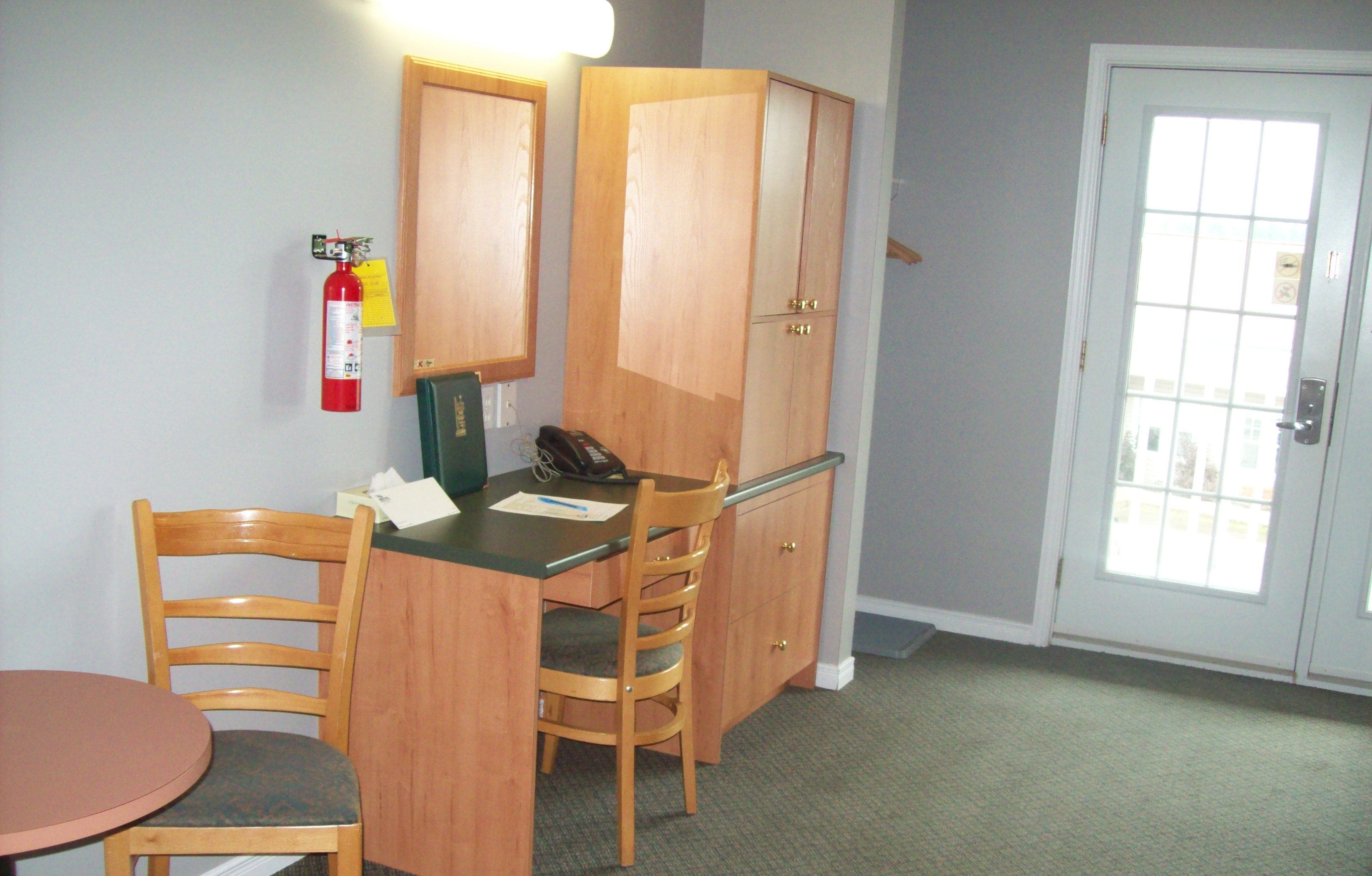 A small room with a wooden desk, two chairs, a telephone, and a fire extinguisher on the wall.