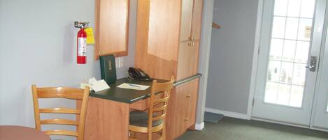 A small room with a wooden desk, two chairs, a telephone, and a fire extinguisher on the wall.