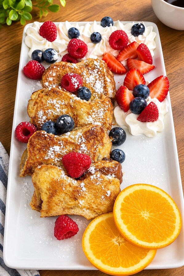 A plate of French toast with whipped cream, berries, and orange slices. - Hill Top Motel & Restaurant (Grand Falls)