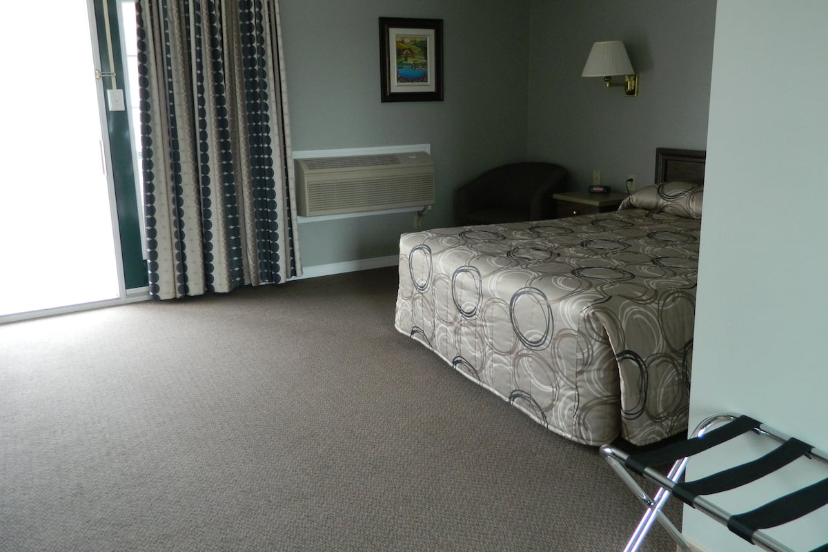 Una habitación de hotel con cama, una silla, un escritorio, una lámpara y una ventana con cortinas.