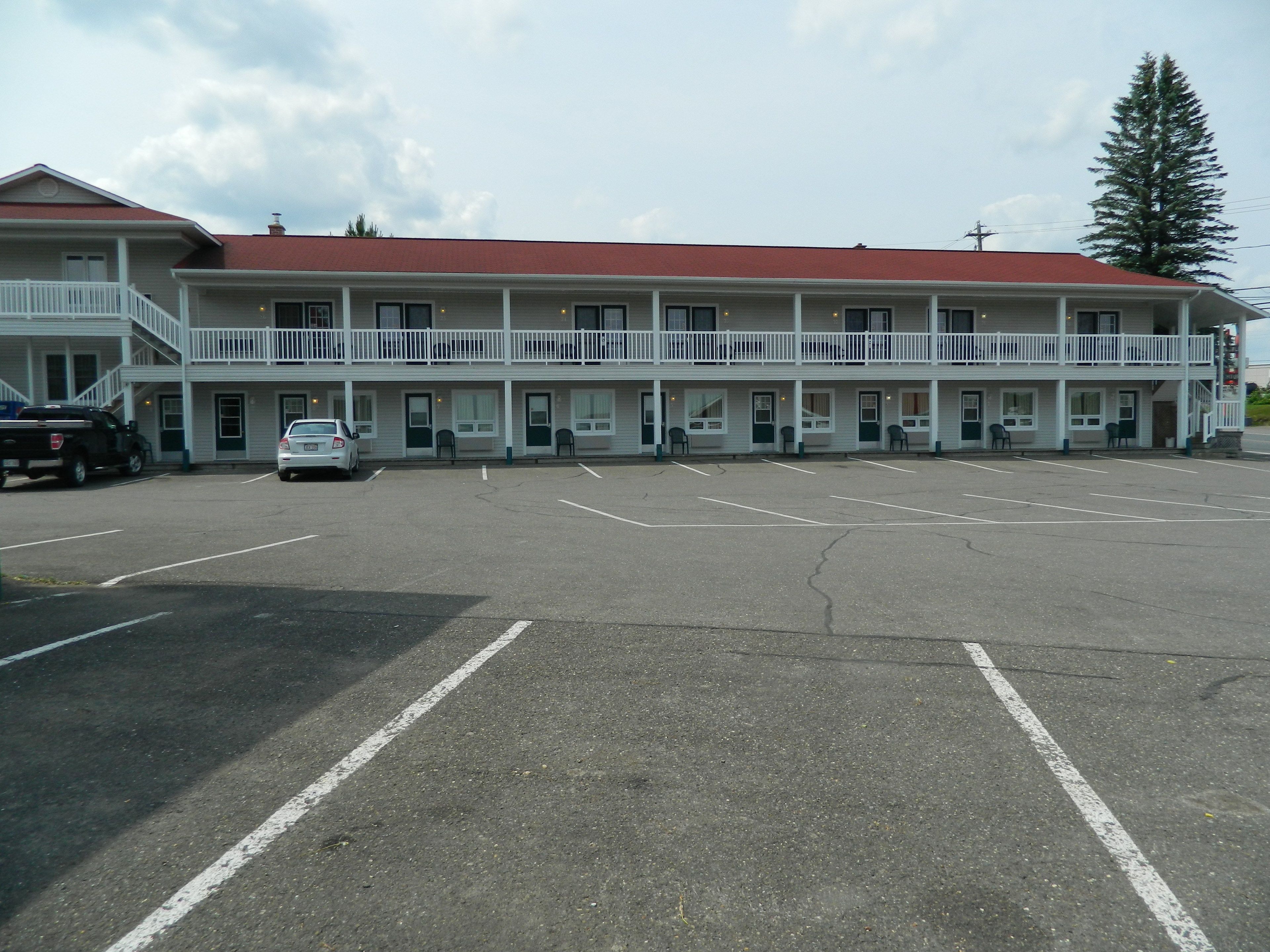 A motel with a red roof and white exterior, featuring a parking lot and a building with multiple balconies.
