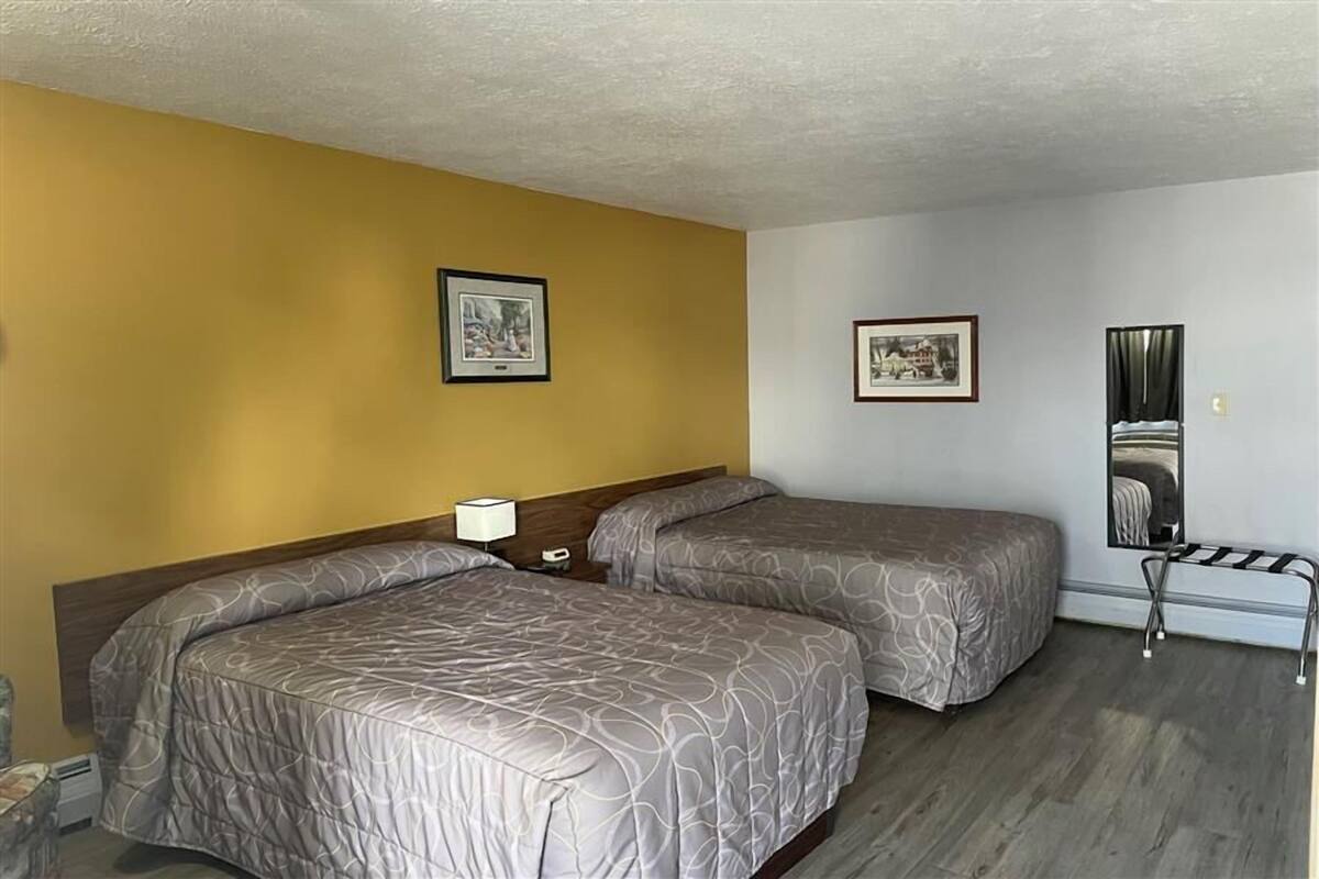 Habitación de hotel con dos camas, una mesita de noche, una lámpara y dos cuadros en la pared.