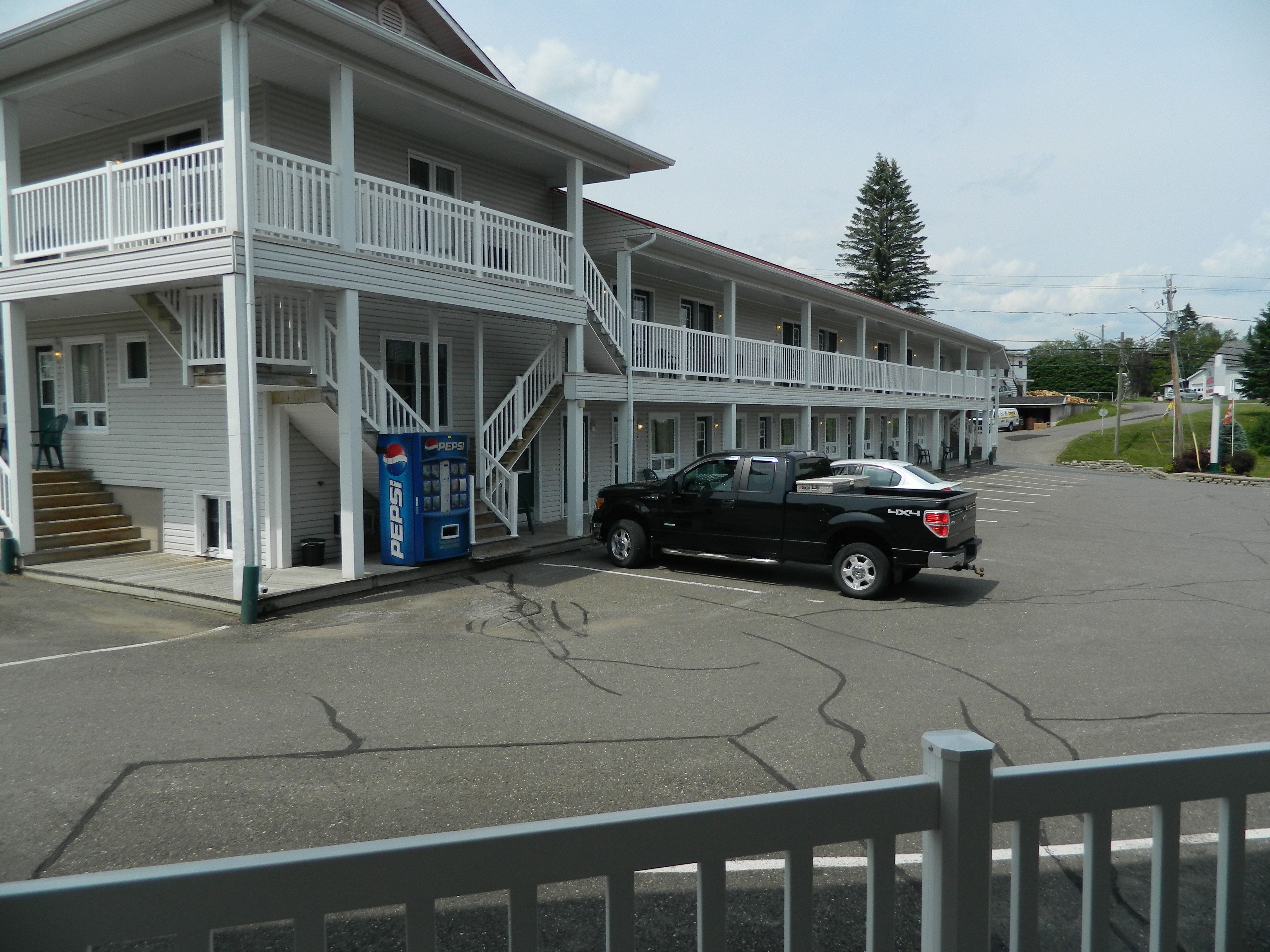 Un motel à deux étages, doté d’un porche avant couvert et d’un escalier menant à l’étage supérieur. Un camionnette noire est garée devant.