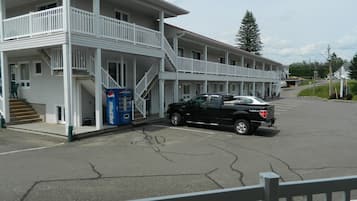 Un motel à deux étages, doté d’un porche avant couvert et d’un escalier menant à l’étage supérieur. Un camionnette noire est garée devant.