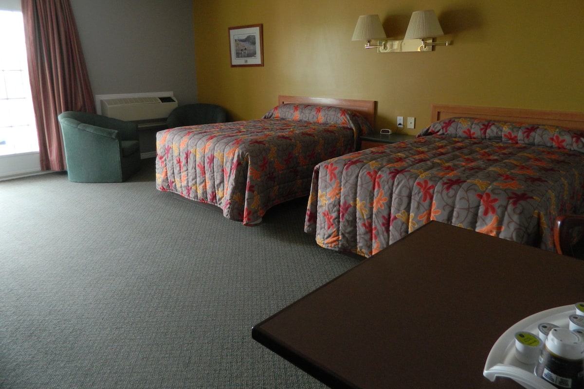 Habitación de hotel con dos camas, un escritorio, una silla y una ventana con cortinas.