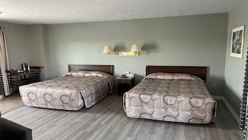 A hotel room with two beds, a desk, a chair, and a lamp.
