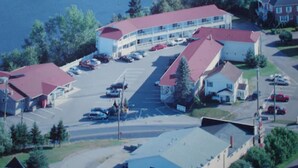 An aerial view of a coastal building complex with multiple parking lots and a marina. - Hill Top Motel & Restaurant (Grand Falls)