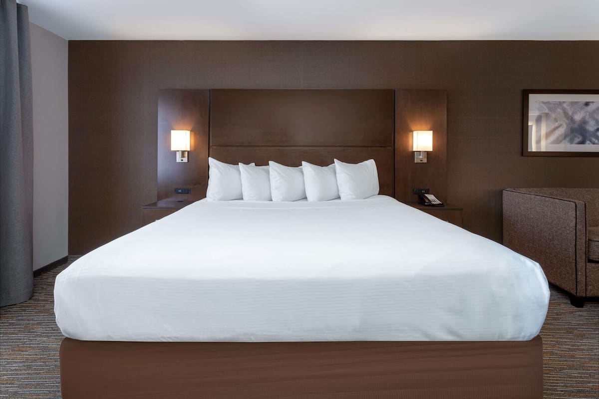 A large bed with a headboard, two bedside lamps, a telephone, and a framed picture on the wall.