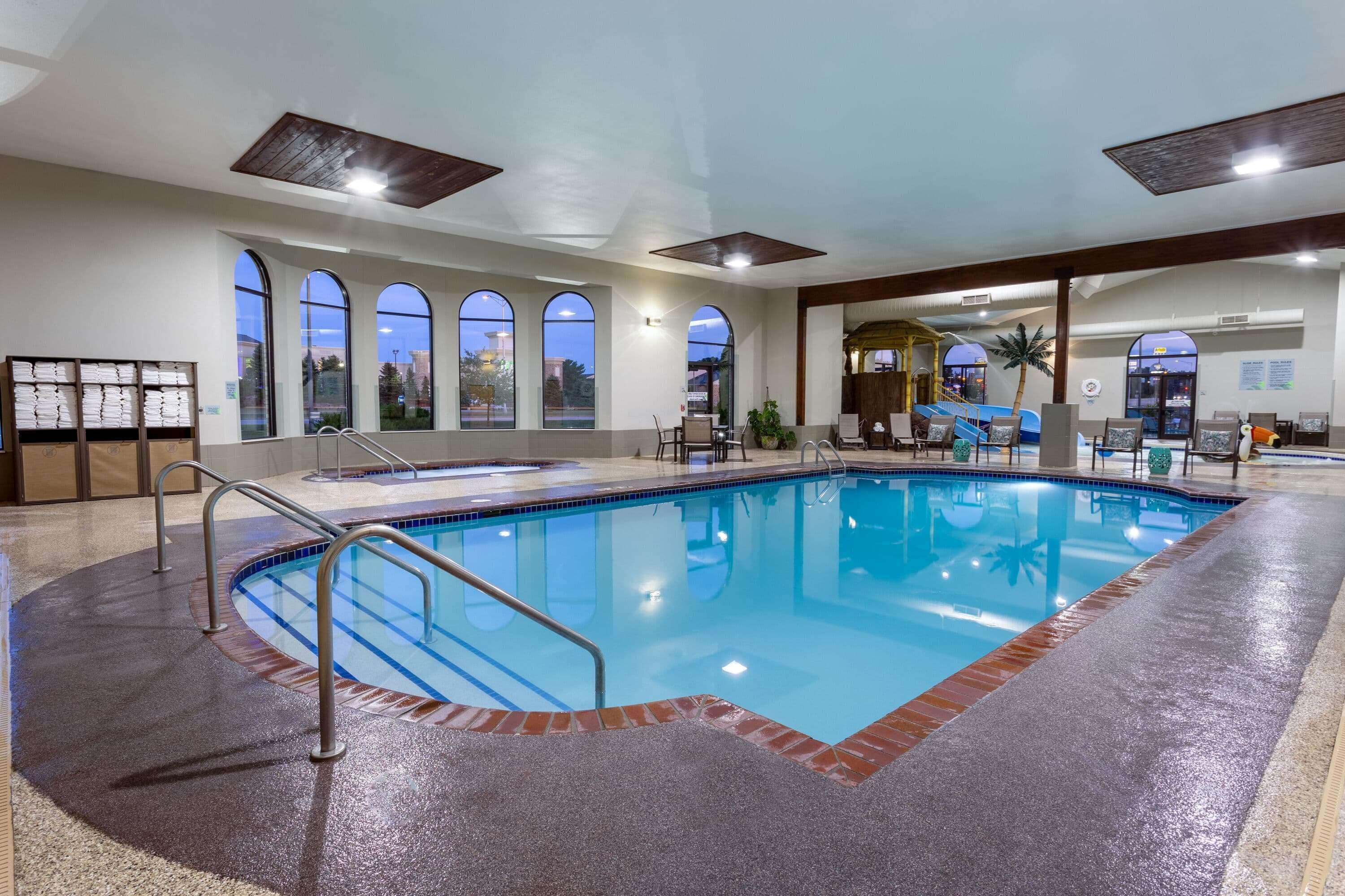 An indoor swimming pool with clear glass walls, a tiled floor, and a wooden ceiling.