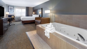 A modern hotel room with a large bed, a sitting area with a chair, a desk with a computer, and a large bathtub with towels. - Wingate by Wyndham Wisconsin Dells Waterpark (Baraboo)