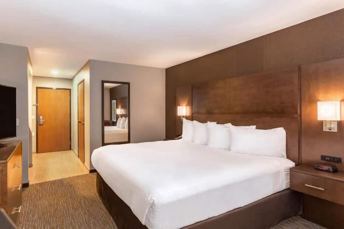 A hotel room with a large bed, a television, a desk, and a mirror.