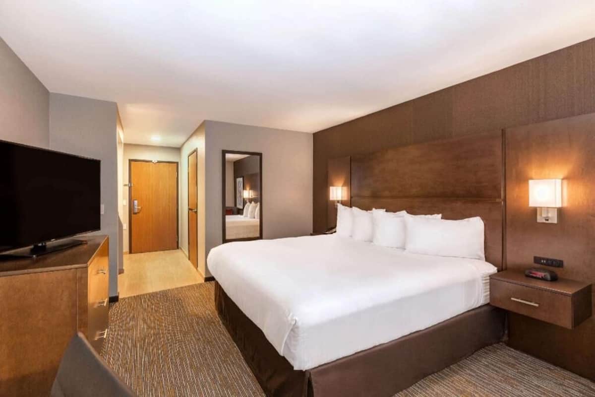 A hotel room with a large bed, a TV, a mirror, and a nightstand with a lamp.