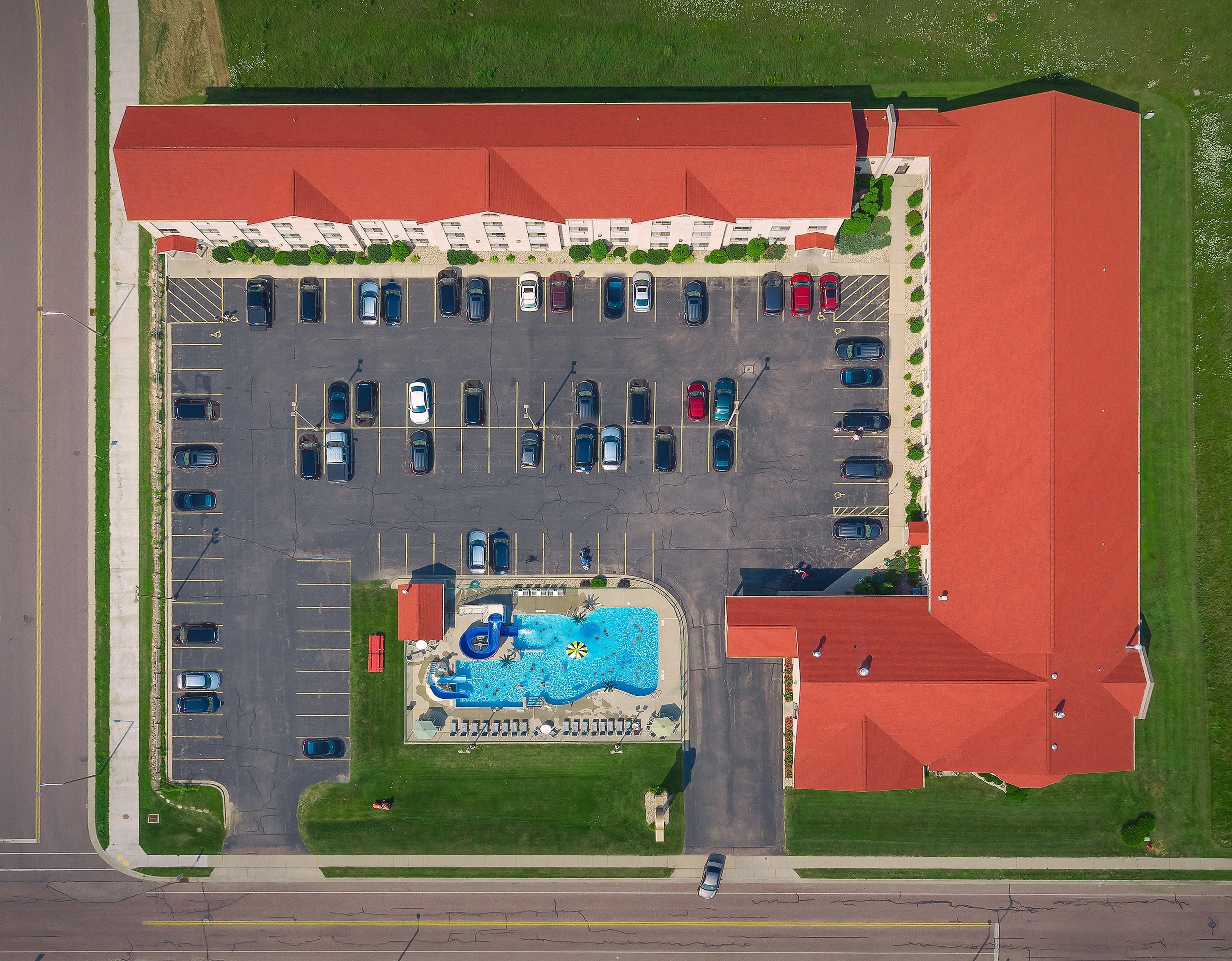 Une vue aérienne d’un parking avec une piscine et un bâtiment doté d’un toit rouge.
