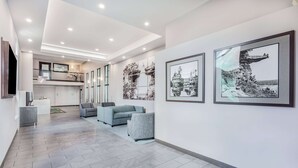 A modern interior with a spacious hallway, grey tiled flooring, a grey sofa, and framed black-and-white photographs on the walls. - Wingate by Wyndham Wisconsin Dells Waterpark (Baraboo)