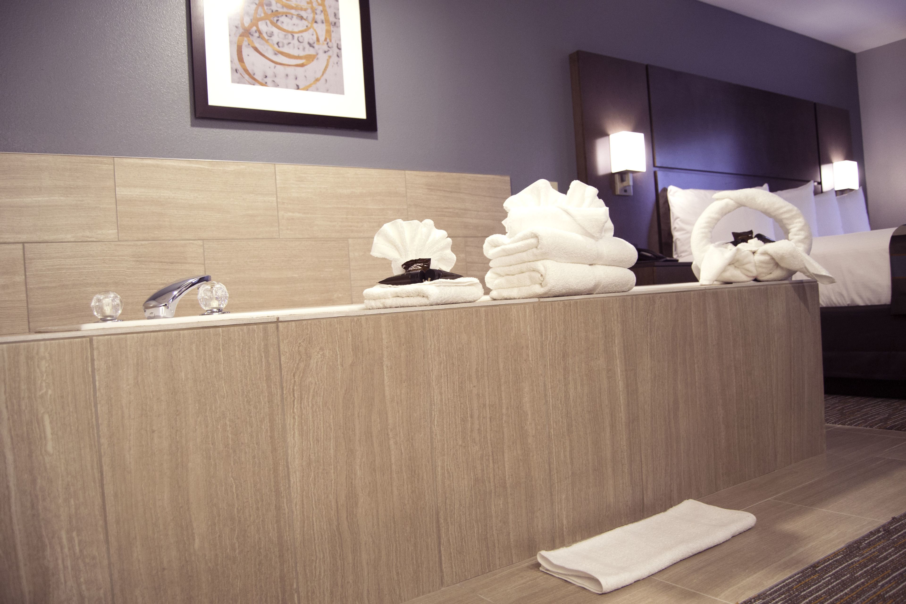 A hotel bathroom with a wooden vanity, a sink, and a bed with a headboard.