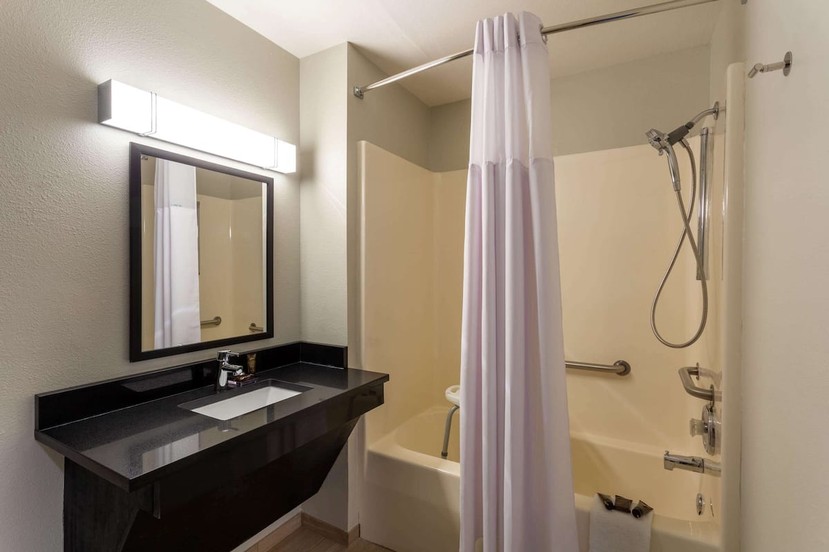 A bathroom with a black sink, a mirror, a shower with a curtain, and a bathtub.