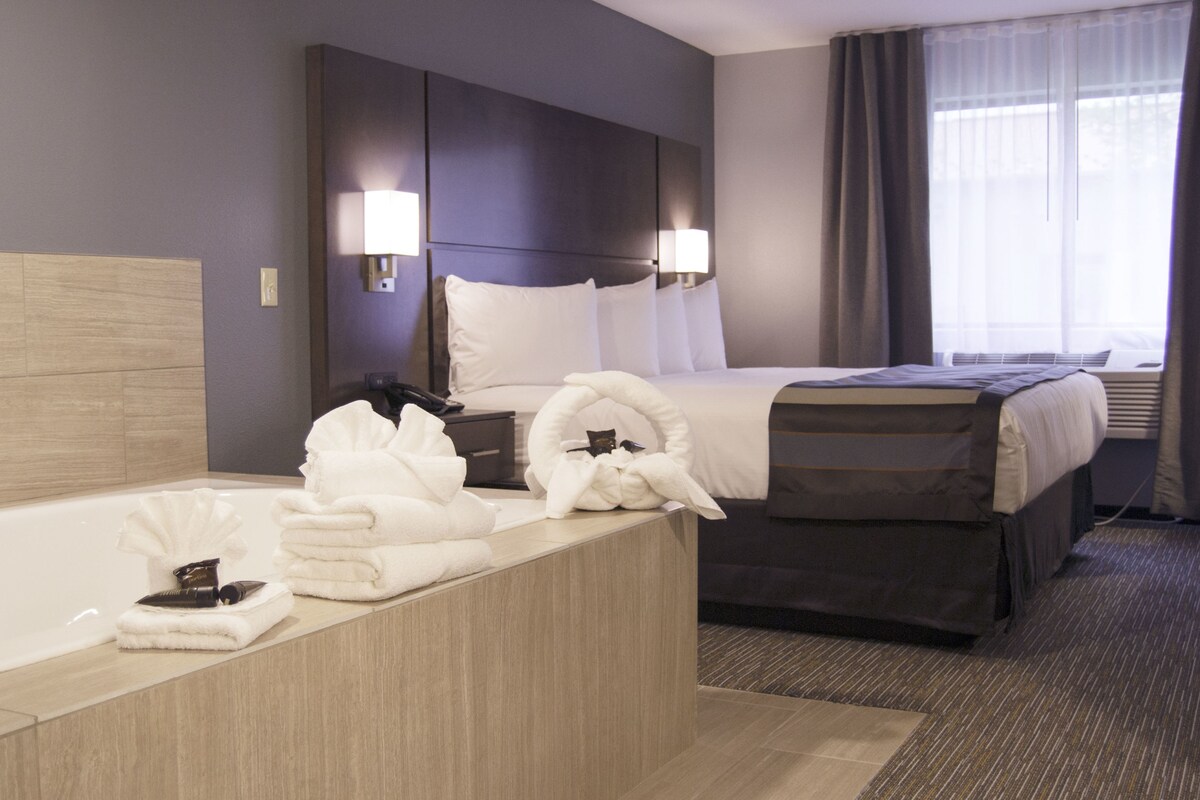 Une chambre d’hôtel dotée d’un grand lit, d’un canapé-lit séparé, d’une salle de bain avec baignoire, et d’un bureau avec des serviettes et des articles de toilette.