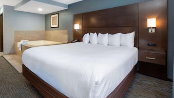 Una cama grande con cabecera de madera, una mesita de noche con lámpara y un baño pequeño con bañera y toallas.