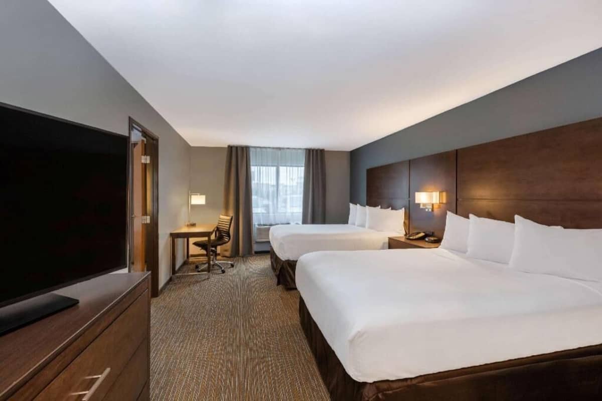 A hotel room with two beds, a TV, a desk, and a lamp.