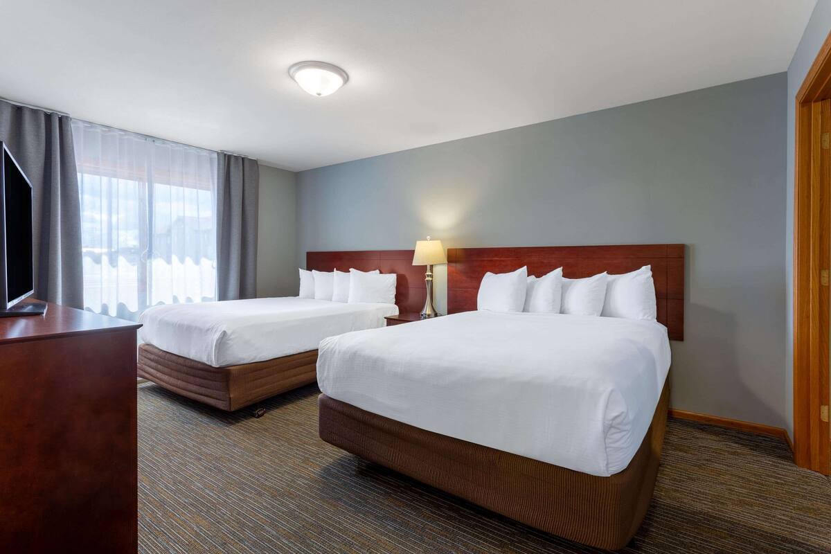 A hotel room with two beds, a desk, a lamp, and a television.