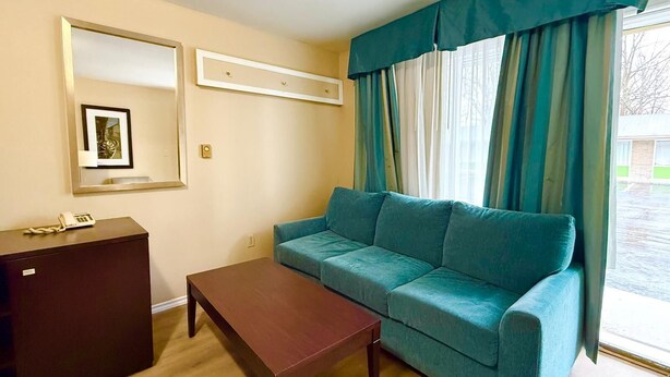 Une pièce avec un canapé de couleur turquoise, une table basse en bois, une commode en bois foncé, un tableau encadré accroché au mur et une fenêtre avec des rideaux.
