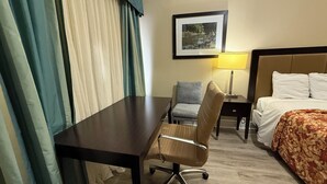 Une chambre d’hôtel avec un lit, un bureau, une chaise, une lampe et des rideaux.