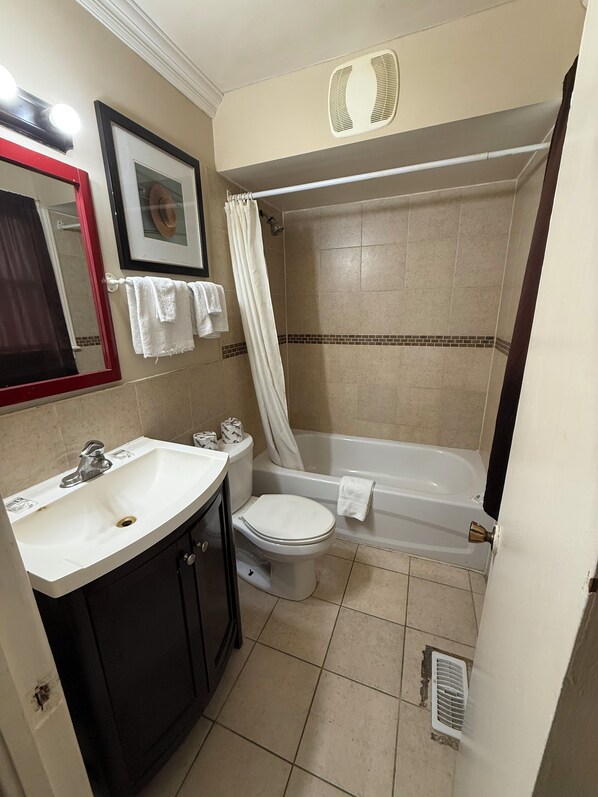 A bathroom with a sink, toilet, bathtub, and shower curtain. - Mohawk Motel (Brantford)