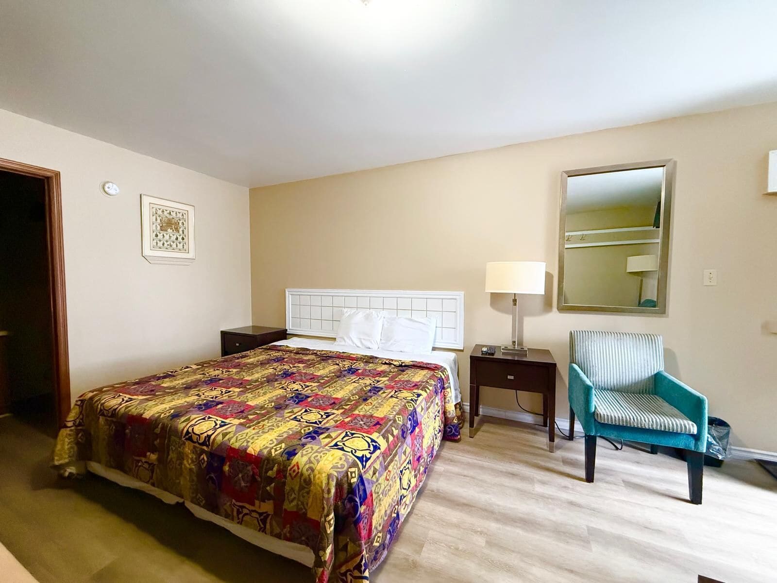A hotel room with a large bed, a bedside table with a lamp, a chair, and a mirror on the wall.