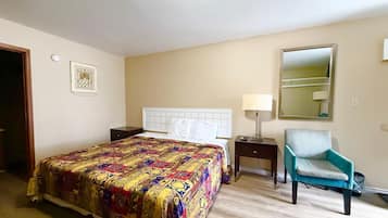 Een hotelkamer met een groot bed, een nachtkastje met een lamp, een stoel en een spiegel aan de muur.