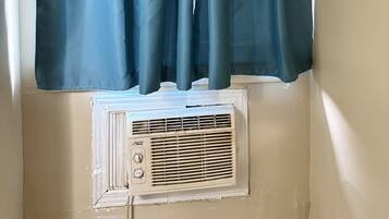 A window with a dark blue curtain and a white air conditioning unit below it.