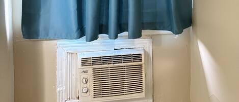 A window with a dark blue curtain and a white air conditioning unit below it.