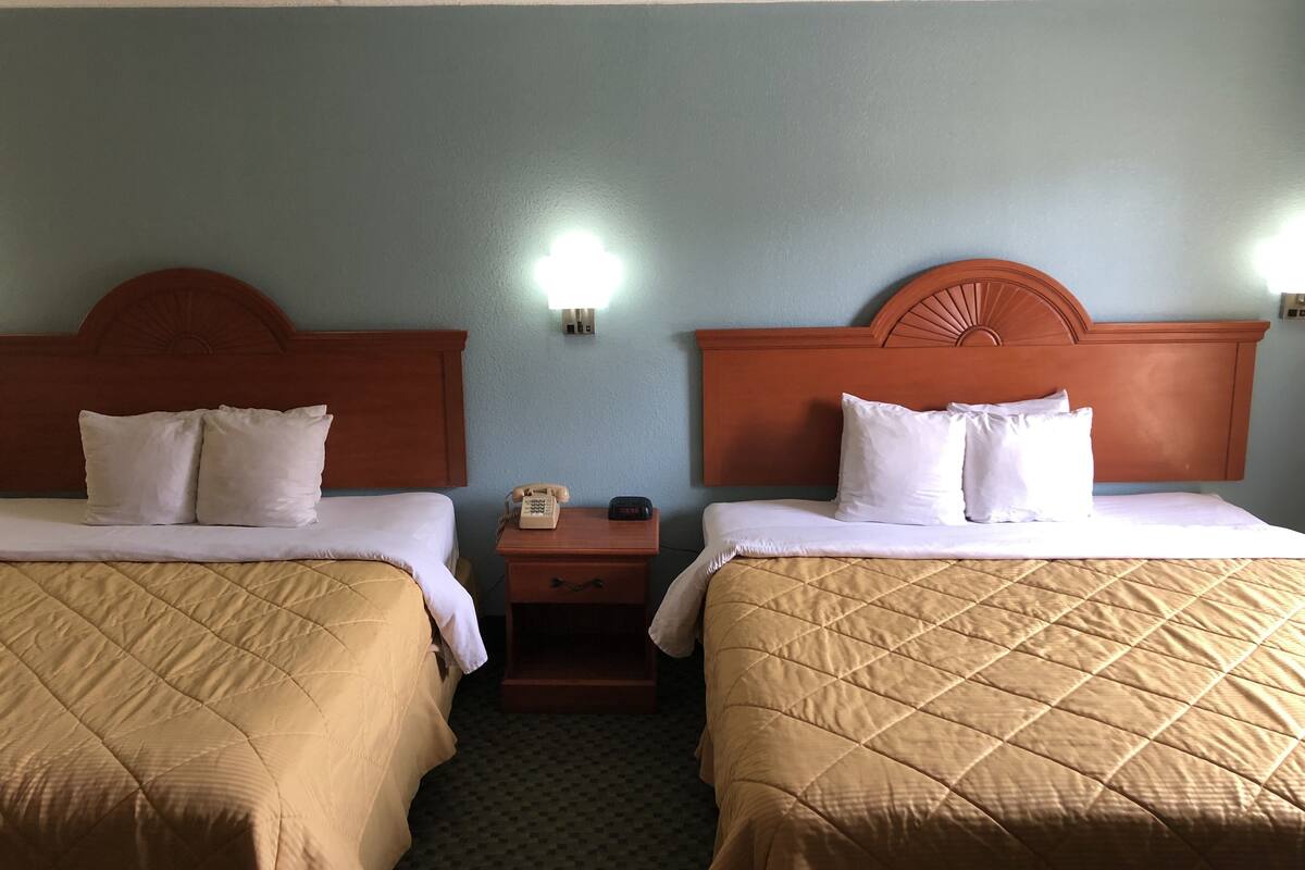 A hotel room with two beds, each with a wooden headboard, a nightstand with a telephone, and a wall-mounted light.