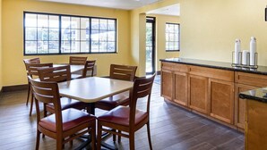 Uma sala de jantar com uma mesa redonda e cadeiras de madeira, uma cozinha com armários de madeira e amplas janelas que permitem a entrada de luz natural.