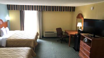 A hotel room with two beds, a desk, a television, a dresser, and an air conditioning unit.
