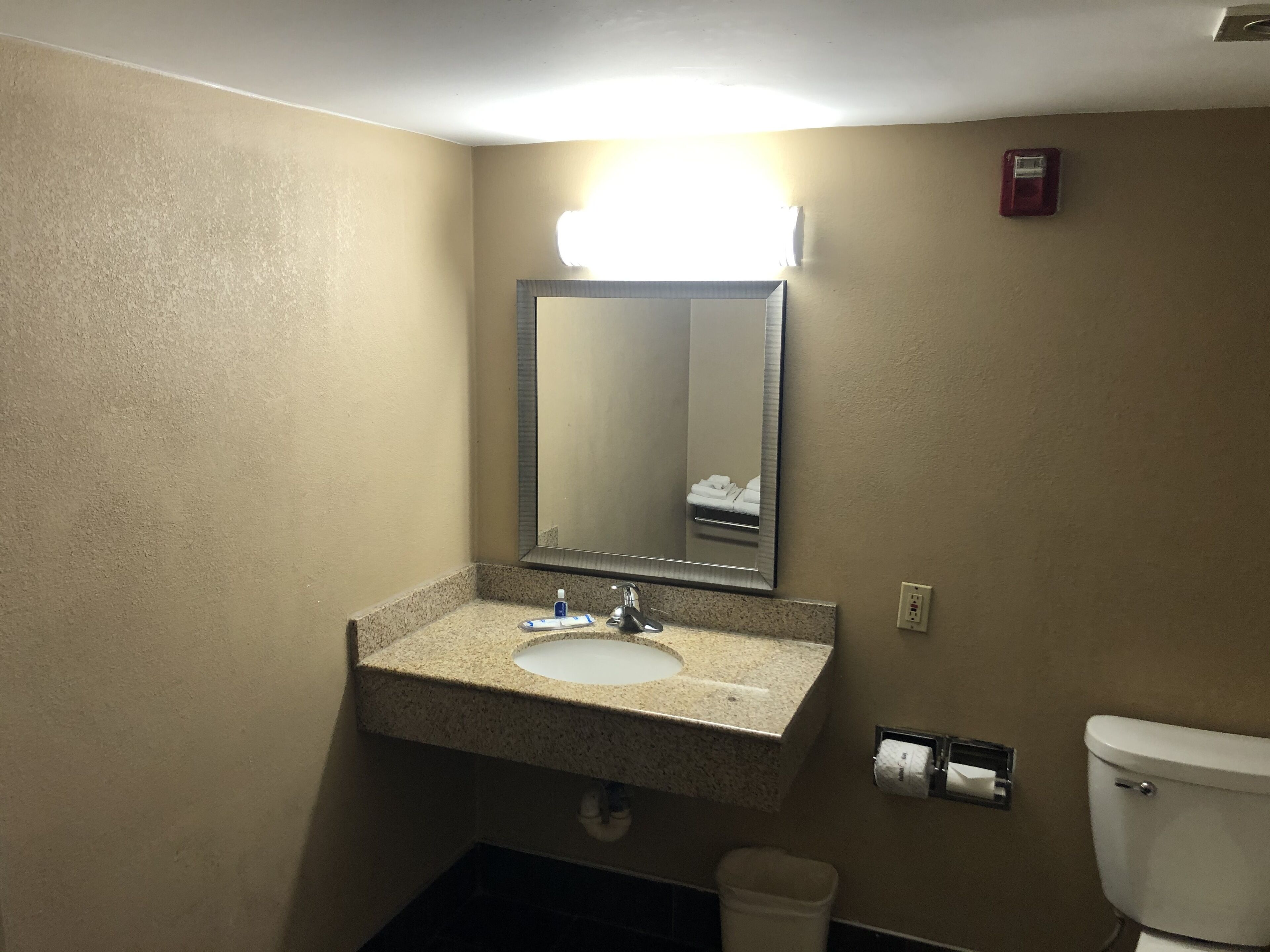 Ein Badezimmer mit Granitwaschtisch, Spiegel, Handtuchhalter, Toilette und Mülleimer.