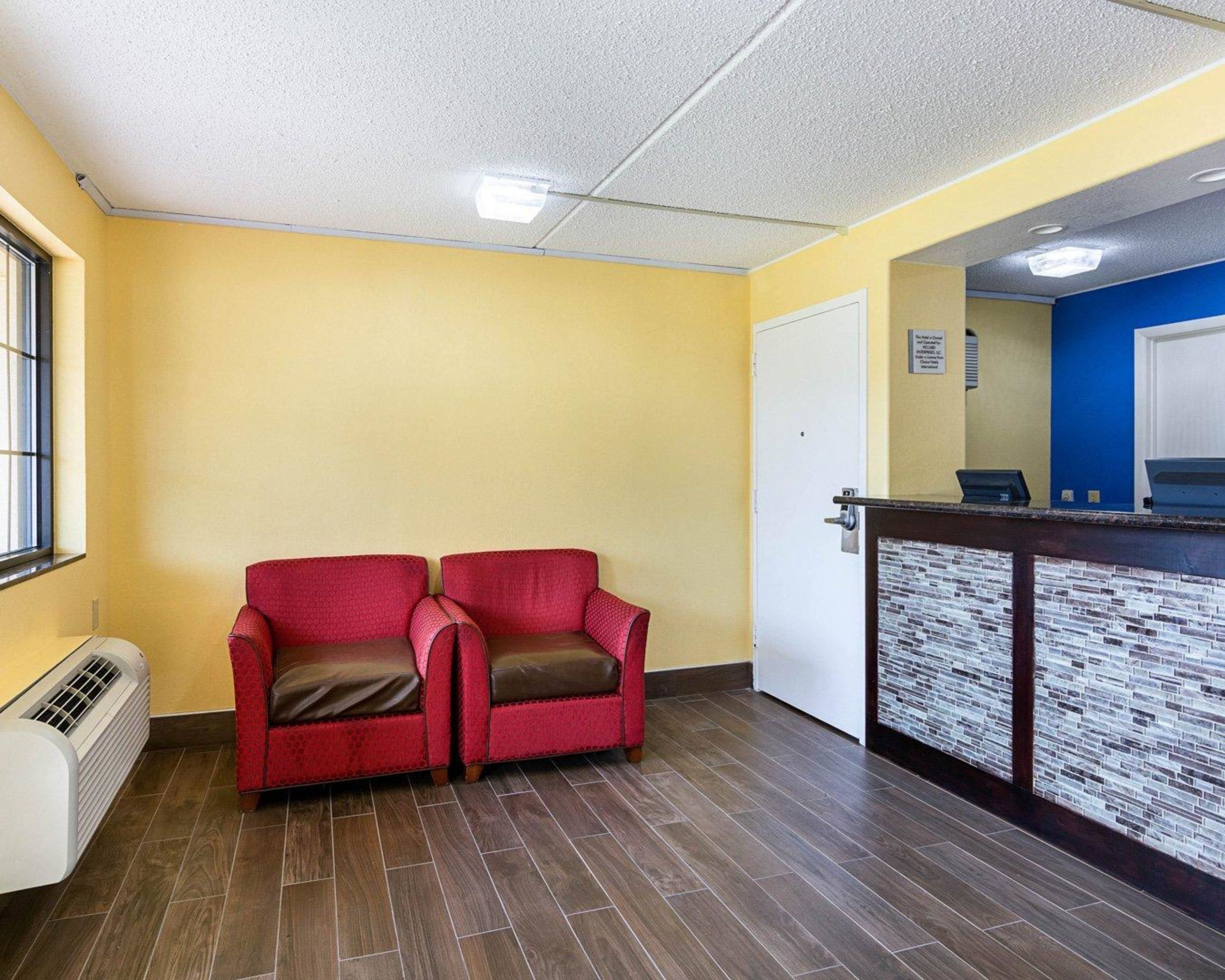 A reception area with a reception desk, two red armchairs, a white door, and a window with blinds.