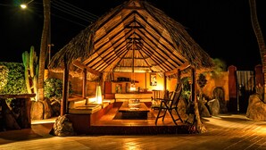 A thatched-roof structure with a wooden deck, seating area, and a table with chairs. - Sea Breeze Apartments (Savaneta)