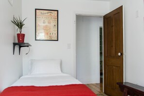 A bedroom with a bed, a red throw blanket, a potted plant, and a poster on the wall.
