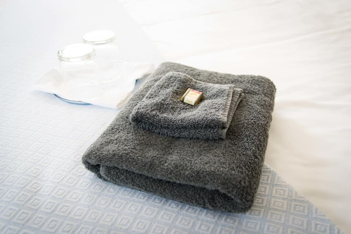 Une serviette grise, soigneusement pliée, est posée sur un lit recouvert d’une couverture bleue à motifs.