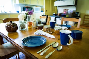 A wooden dining table with blue plates, silverware, and a blue mug.