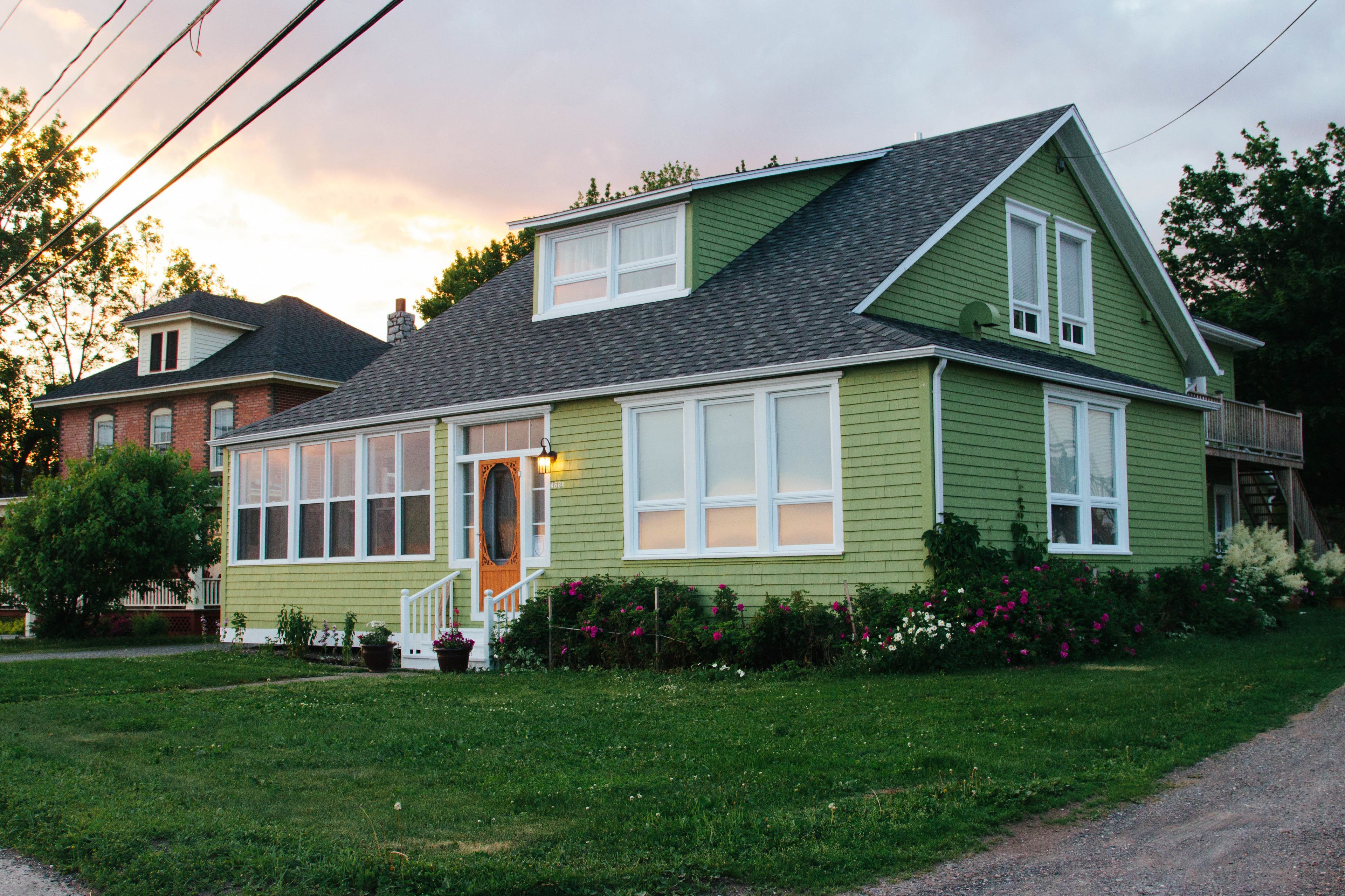 A green house with a front porch, large windows, and a well-maintained lawn.