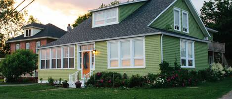 A green house with a front porch, large windows, and a well-maintained lawn.