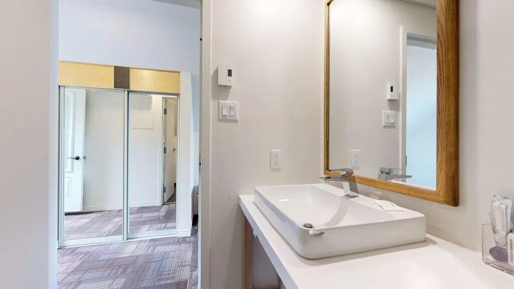 Un baño moderno con un espejo grande, un lavabo blanco y una cabina de ducha de vidrio.