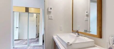 Un baño moderno con un espejo grande, un lavabo blanco y una cabina de ducha de vidrio.